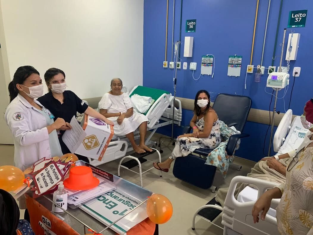 As coordenadoras do Núcleo de Segurança do Paciente Isabelle Diniz e do Núcleo de Educação Permanente Rebeca Cutrim aplicando jogos educativos com pacientes e acompanhantes no HSE.