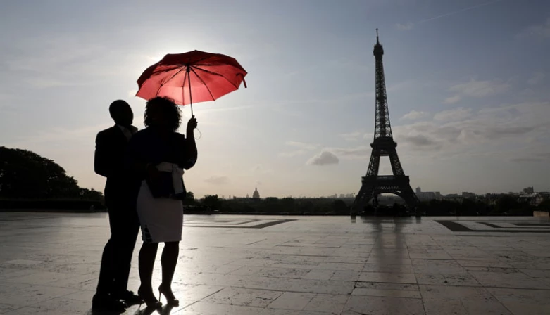 Um casal com um guarda-chuva observa o nascer do sol na Praça do Trocadero, perto da Torre Eiffel